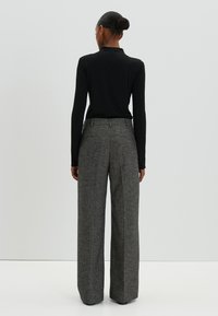 Zwarte lange mouwen top gecombineerd met hoge taille, wijde grijze broek. De broek heeft een gestructureerde stof en twee achterzakken.