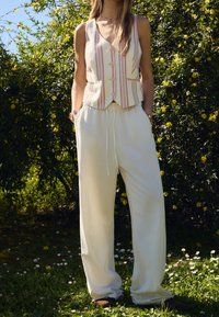 Pantaloni bianchi a gamba larga con vita elastica, abbinati a un gilet a righe in colori chiari con bottoni e design a V.