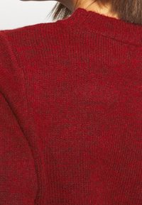 Pull en tricot rouge avec un tissu texturé, un col côtelé et une coupe ajustée avec un motif ton sur ton subtil.