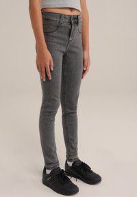 Grå skinny jeans med en klassisk design, hög midja och subtil blekning, matchade med svarta sneakers i texturerat material och snörning.