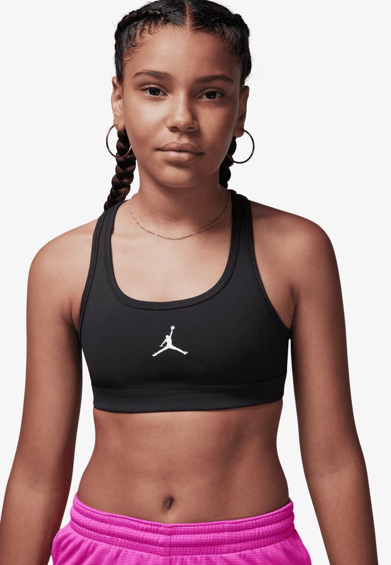 Sutien sport negru cu bretele late și logo Jordan alb. Textură netedă. Asortat cu pantaloni scurți roz cu șnur și talie striată.