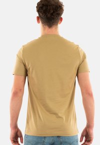 Camiseta de manga corta y cuello redondo en color beige, hecha de algodón suave, con una textura lisa y un diseño ajustado con detalles de costura mínimos.