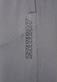 Szare spodnie sportowe z teksturowanej tkaniny, z czarnym logo "HUMMEL" nadrukowanym na boku oraz bezszwowym wzorem.