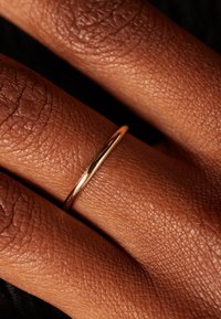 Gold ring featuring a smooth, thin band resting on a hand, highlighting a textured skin surface and rich skin tones.