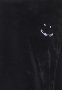 T-shirt en velours noir avec un logo visage souriant brodé en blanc et le texte « Paul Smith ». Le tissu a une texture douce et pelucheuse.