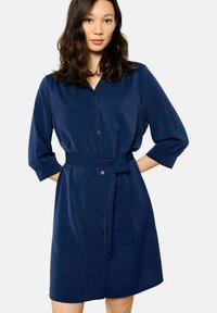 Robe chemise bleu marine en tissu lisse, dotée d'un devant à boutons, d'un col, d'une ceinture à la taille et de manches trois-quarts.