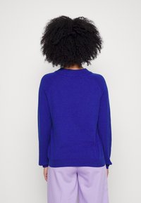 Blå-lila tröja med rundad hals och långa ärmar, med en slät textur och ribbade detaljer vid ärmsluten och nederkanten.