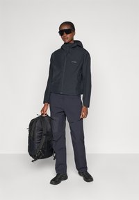 Black waterproof jacket with hood, matching dark pants, and sturdy black backpack. Features a slim fit, smooth texture, and minimalist design.