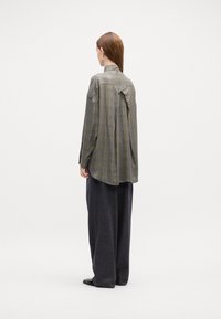 Camicia oversize a quadri grigia e gialla con uno spacco sul retro, maniche lunghe e colletto con bottoni, indossata con pantaloni larghi grigio scuro.