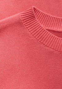 Pull en maille rose clair avec un col côtelé et une texture. Le design présente une finition douce et lisse ainsi que des lignes épurées.
