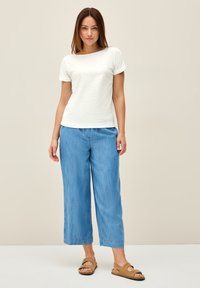 Hvid tekstureret kortærmet bluse kombineret med lyseblå vide bukser og brune sandaler. Enkel design med afslappet pasform og casual stil.