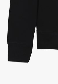 Černá mikina s ribovanými manžetami, hladkým povrchem a čistým lemem. Materiál vypadá měkce a elasticky.