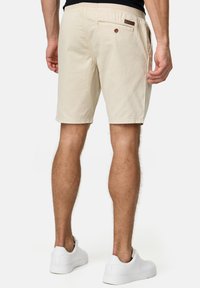 Beige bomuldsshorts med en afslappet pasform, der har en baglomme med knaplukning og et lille mærke. Bæres med hvide sneakers.