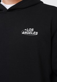 Sudadera negra de algodón con un logo bordado en blanco que dice "LOS ANGELES" y un acento de estrella, diseñada con un corte clásico y una textura suave.