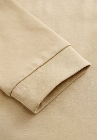 Beženi dukserica od tkanine s dizajnom preklopnog manšeta, glatkom teksturom i suptilnim rebrastim detaljem na rubu rukava.