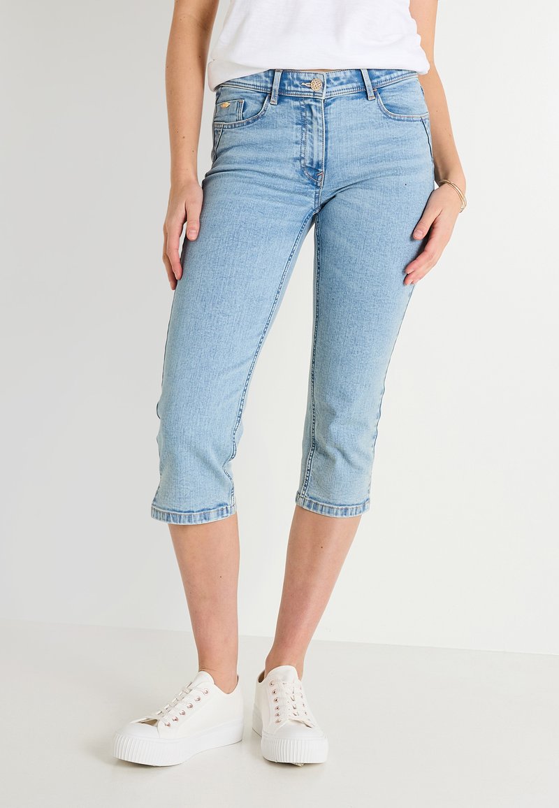 Jeans capri de denim azul claro con un ajuste ceñido, cintura de altura media y dobladillo enrollado, combinados con zapatillas de plataforma blancas.
