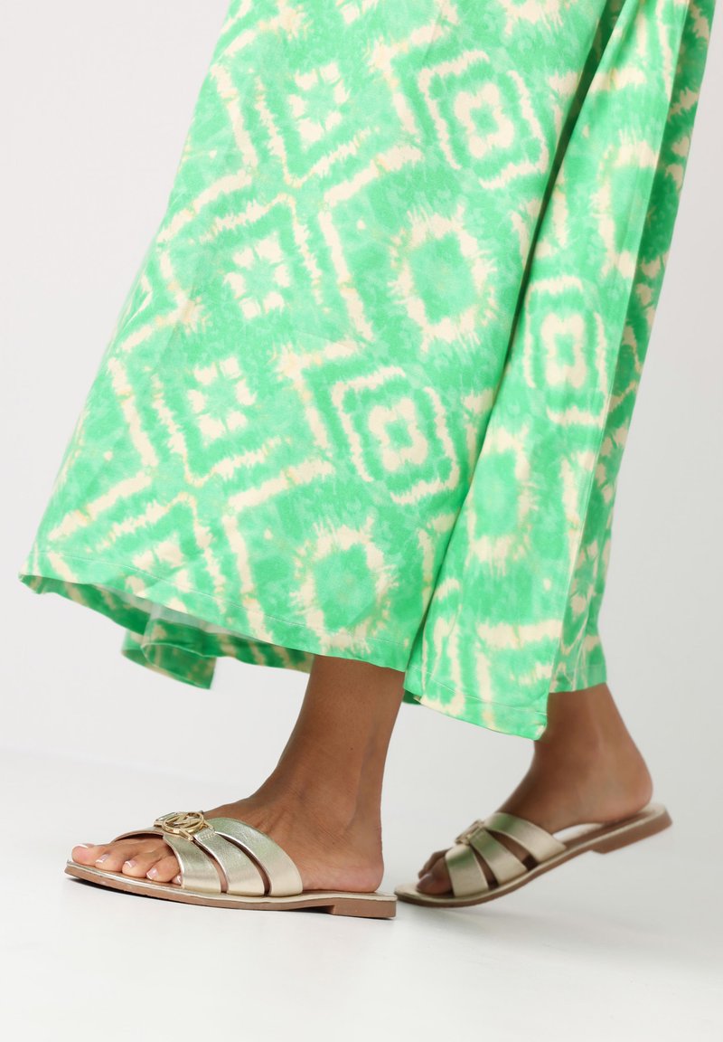 Gouden slide sandalen met drie brede banden. Tan zool. Draag met een groene tie-dye maxi-jurk met een geometrisch patroon.