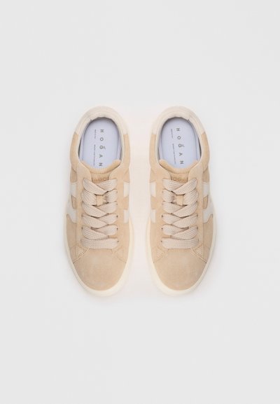 Baskets en suede beige avec bouts arrondis, lacets texturés et accents sur les côtés. Semelles en caoutchouc blanche et branding sur la semelle intérieure visibles.
