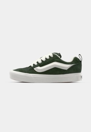 Groene suede sneaker met witte veters en een zijstreep, met een laag profiel, ronde neus en een gestructureerde witte rubberen zool.