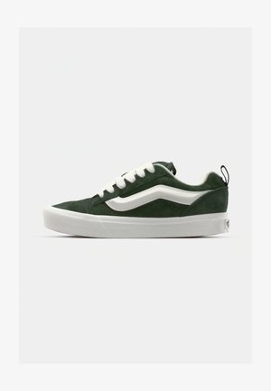 Zapatillas de ante verde con cordones blancos y una franja lateral, con un perfil bajo, punta redondeada y una suela de goma blanca texturizada.