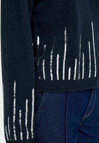 Marineblauwe trui van textuurstof, met verticale zilveren pailletten langs de zoom en mouwen, die een decoratief patroon creëren.