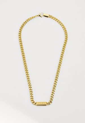 Zlatý náhrdelník s tlustými články, který obsahuje obdélníkový přívěsek s vyrytým nápisem "GUESS." Hladký kovový povrch, uzávěr na klips.