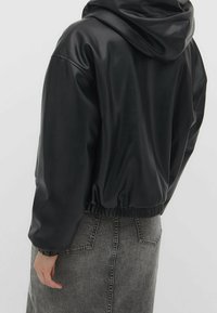 Veste courte en simili cuir noir avec capuche, ourlet et poignets élastiqués. Texture lisse avec un design minimaliste.