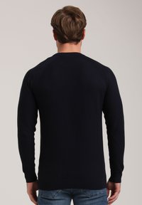 Dunkelblauer strukturierter Pullover mit langen Ärmeln, gerippten Bündchen und Rundhalsausschnitt, von hinten vor einem hellen Hintergrund gezeigt.