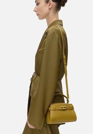 Borsa gialla senape con una forma strutturata, dotata di manico superiore e tracolla regolabile. Realizzata in pelle liscia con dettagli metallici.