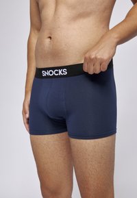 Mörkblå boxershorts med svart elastisk midjeband som har vit "SNOCKS"-logotyp, slät textur och åtsittande design.