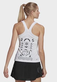 Top in cotone bianco senza maniche con dettagli grafici ritagliati in nero. Presenta un design con schiena a racer e un tessuto texturizzato, abbinato a una gonna nera.