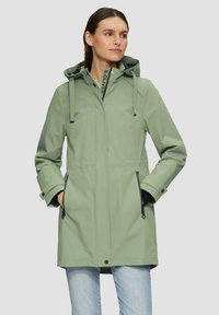 Abrigo impermeable de color verde claro con capucha, que cuenta con bolsillos con cremallera, cordones ajustables y un diseño sencillo. Textura suave.