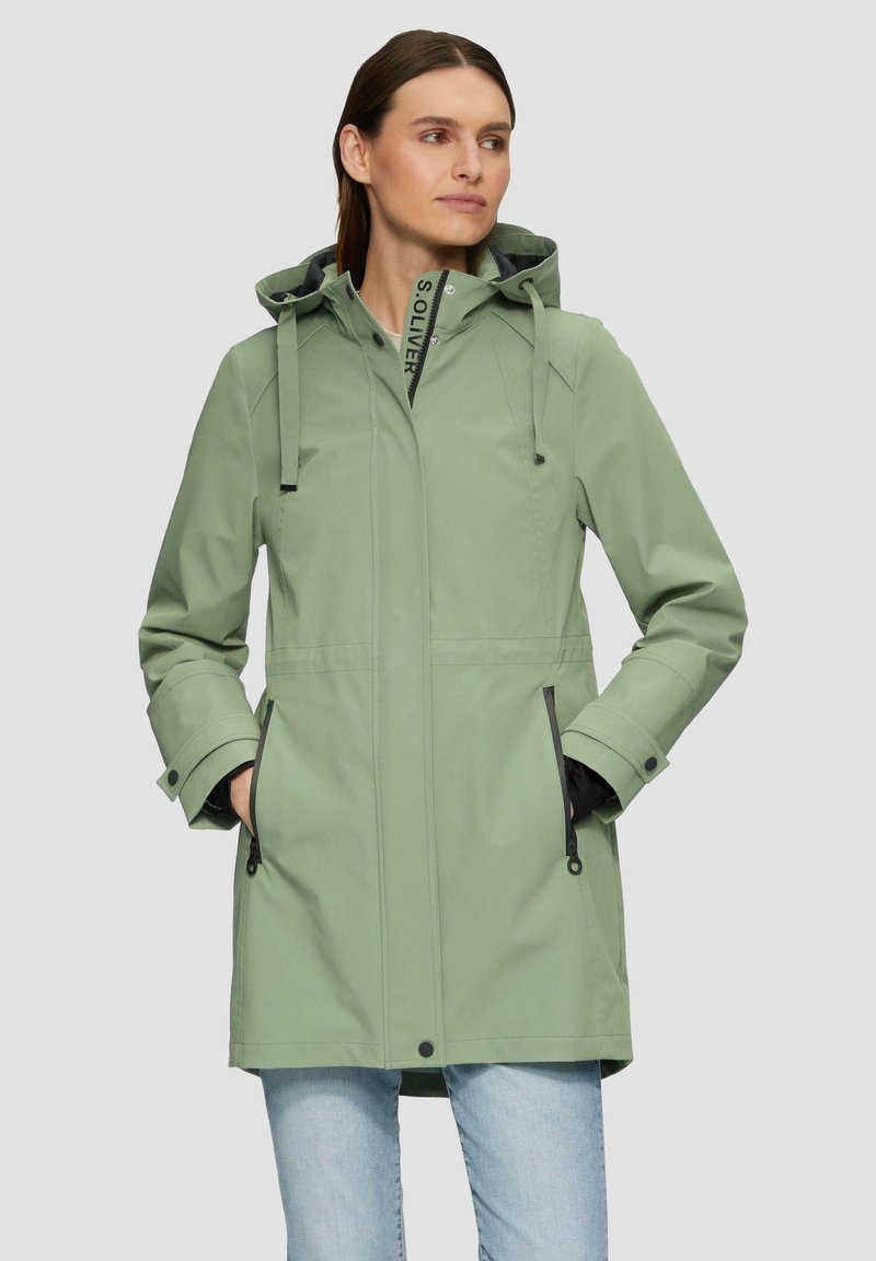 Abrigo impermeable de color verde claro con capucha, que cuenta con bolsillos con cremallera, cordones ajustables y un diseño sencillo. Textura suave.
