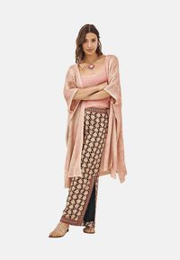 Cárdigan de punto rosa claro sobre una blusa rosa, acompañado de pantalones negros con estampado que presentan acentos en beige y rojo. Sandalias de tiras completan el conjunto.