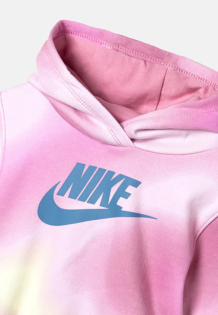 Hoodie présentant un dégradé de teintes roses avec un logo Nike bleu affiché en évidence sur la poitrine. Les textures du tissu doux sont visibles.