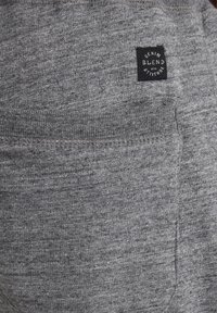 Pantalones jogger de tela gris con un bolsillo trasero y una etiqueta negra que dice "Denim Blend with Attitude". Textura suave y cinturilla elástica.