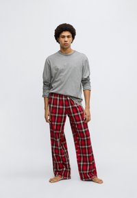 Gray long-sleeve shirt paired with red plaid pajama pants featuring a loose fit, soft fabric, and contrasting checkered pattern. Barefoot stance.