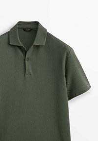Polo shirt vert foncé en tissu texturé, à manches courtes et avec une patte de boutonnage à trois boutons, présentant un col rabattu et une coupe décontractée.