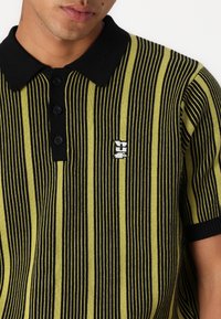 Polo shirt featuring vertical black and neon green stripes, with a black collar and three black buttons. Includes a small white logo detail.