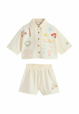 Cremefarbenes Kurzarmhemd mit Kragen und Shorts mit Knopfleiste vorne, bestickt mit Blumen, Sonne, Vogel, Erdbeeren und Schriftzügen auf dem Stoff.