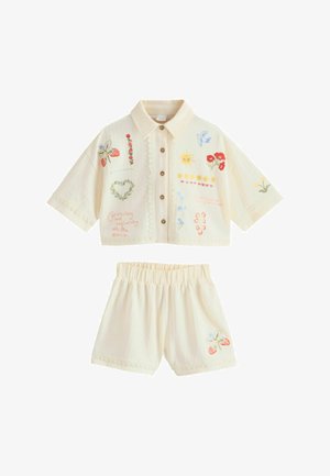Cremefarbenes Kurzarmhemd mit Kragen und Shorts mit Knopfleiste vorne, bestickt mit Blumen, Sonne, Vogel, Erdbeeren und Schriftzügen auf dem Stoff.