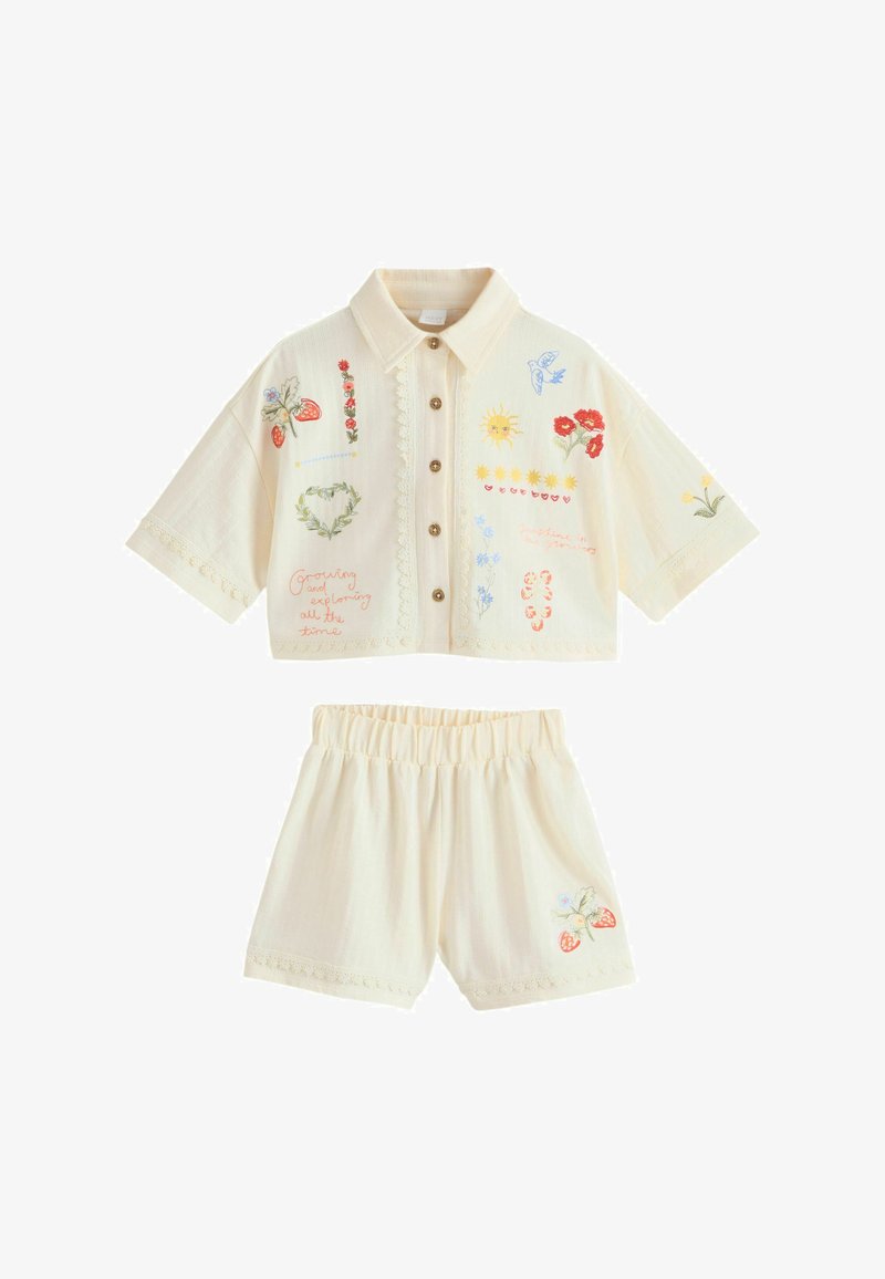 Conjunto de camisa de manga corta con cuello y pantalones cortos en color crema con cierre de botones delantero, bordados con flores, sol, pájaro, fresas y escritos en la tela.