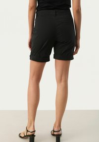 Sorte shorts med oprullede manchetter, lavet af et glat stof, standard talje og baglommer. Bæret med sorte hæle-sandaler.