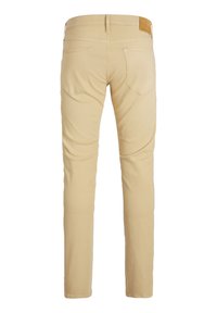 Pantalon beige slim avec deux poches arrière et un patch en cuir marron sur la taille, vu de dos.