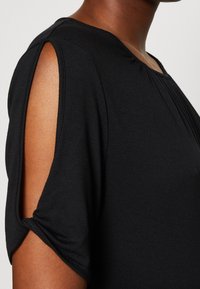 Černý top s krátkým rukávem a výřezem na rameni, měkká textura a řasený výstřih. Vyrobeno z elastického materiálu pro pohodlí.