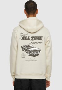 Sudadera color crema con cordón y estampado gráfico que presenta un diseño de coche vintage y texto en la parte posterior. Tejido mezcla de algodón.
