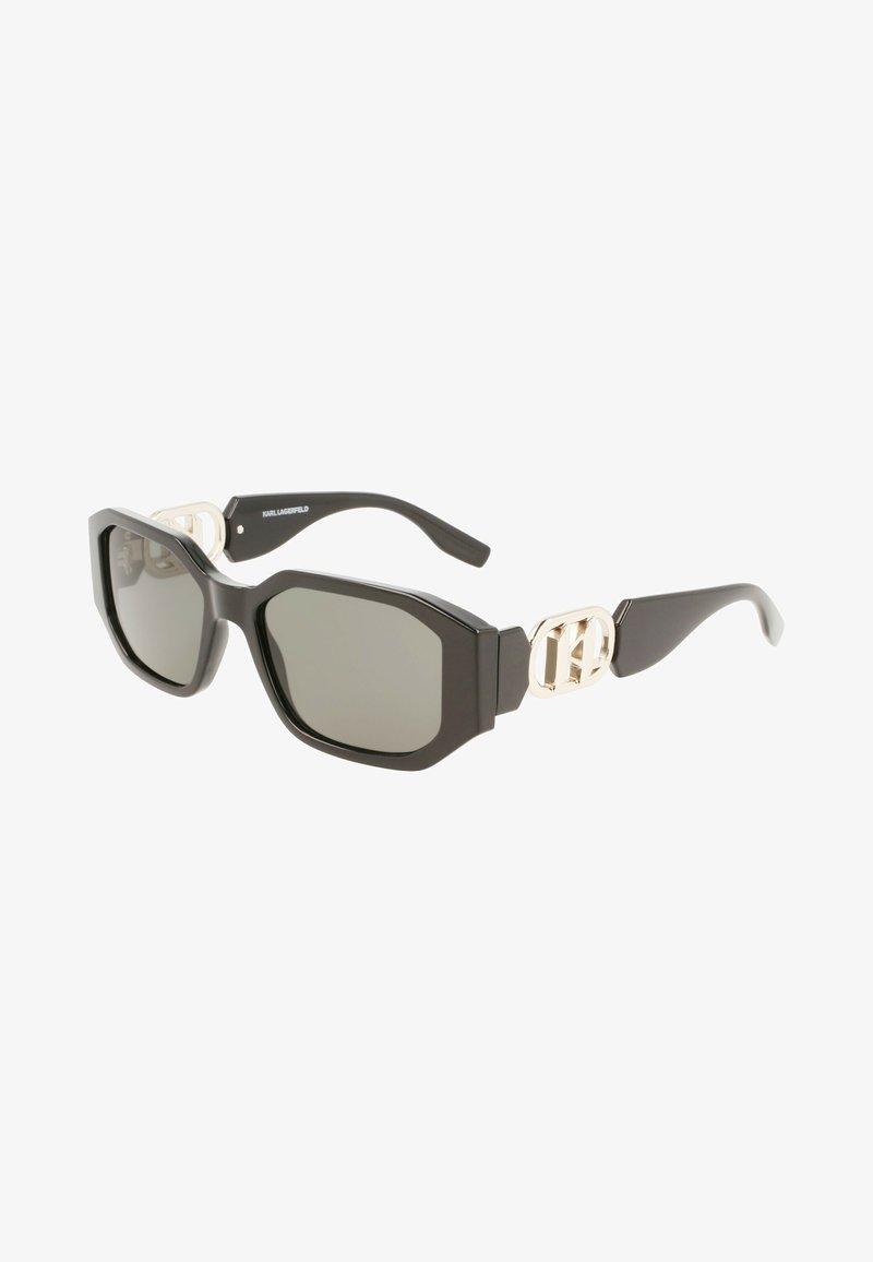 Óculos de sol oversized pretos com lentes escuras, armação angular, detalhe com logotipo dourado nas hastes e textura de superfície lisa.