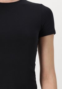 T-shirt noir à manches courtes, fabriqué en tissu doux et extensible. Encolure ras du cou simple, design ajusté avec une texture lisse.