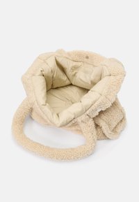 Bolso de mano de pelaje sintético beige con un exterior suave y texturizado, un forro beige liso y dos asas de felpa. El interior cuenta con un bolsillo con cremallera.