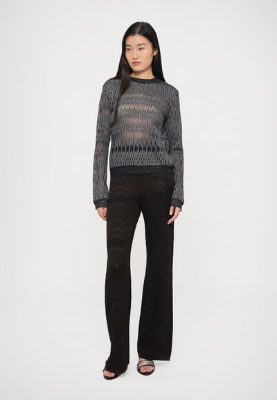 Tamsiai mėlynas ir pilkas megztinis su laisvu siluetu ir gofruotu apačios briaunu, derinamas su juodomis, tekstūruotomis, platėjusiomis kelnėmis, kuriose matomas banguotas raštas.